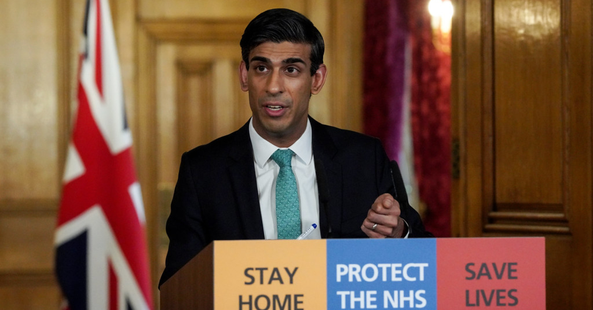 Rishi Sunak behind podium with the words, "Stay home, protect the NHS, Save Lives" on the front