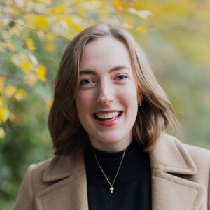 A photo of Lauren McLay smiling into camera dressed smartly with a leafy, autumnal background