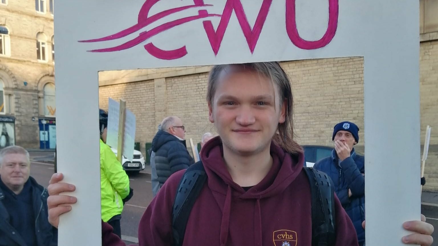 Finn smiling towards camera holding a CWU sign