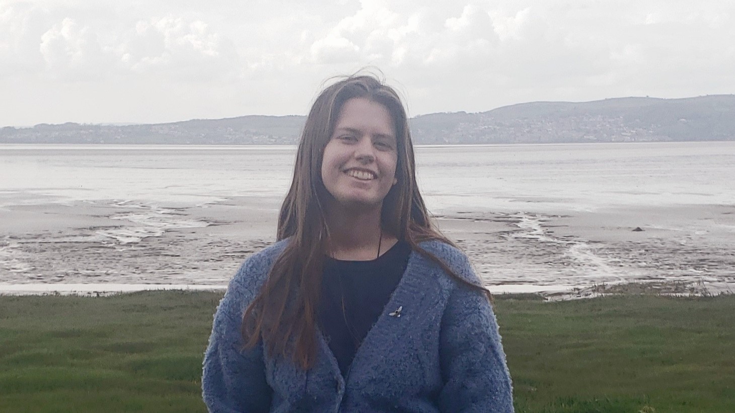 Eleanor smiling broadly to camera with the beach and a sea behind her