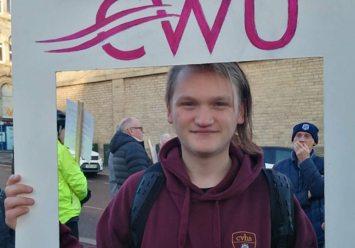 Finn smiling towards camera holding a CWU sign